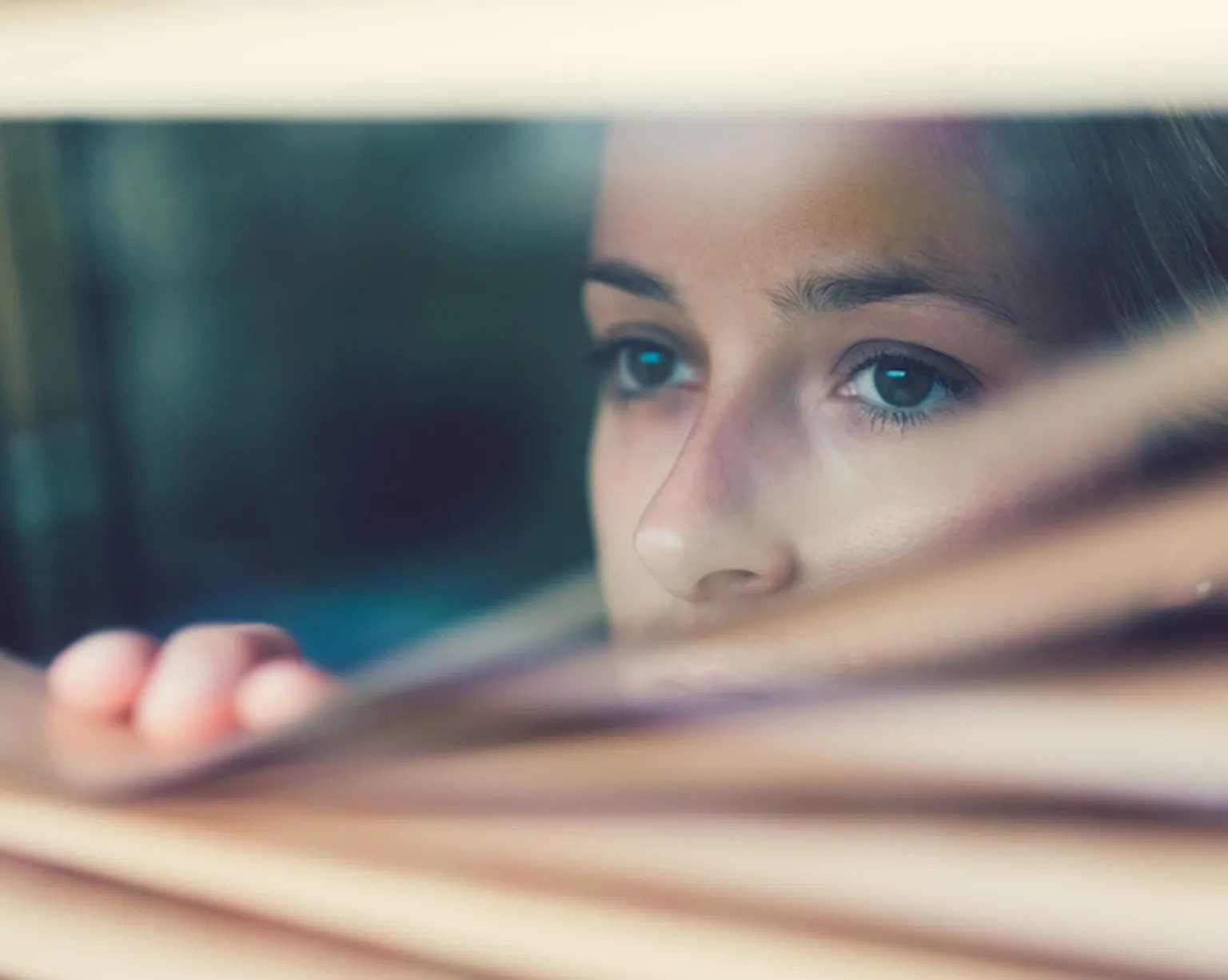 Photo of a young person peering through a window from inside.
